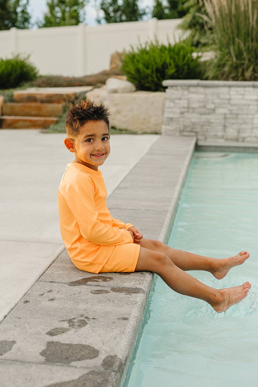 
                  
                    Child in an orange swimsuit sitting by a pool.
                  
                