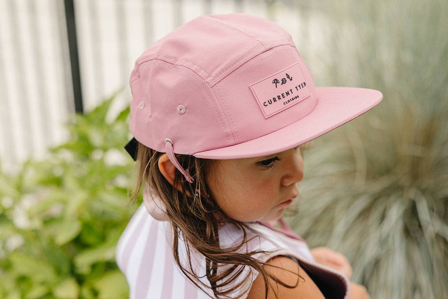 Child wearing a pink cap with text, standing outdoors.