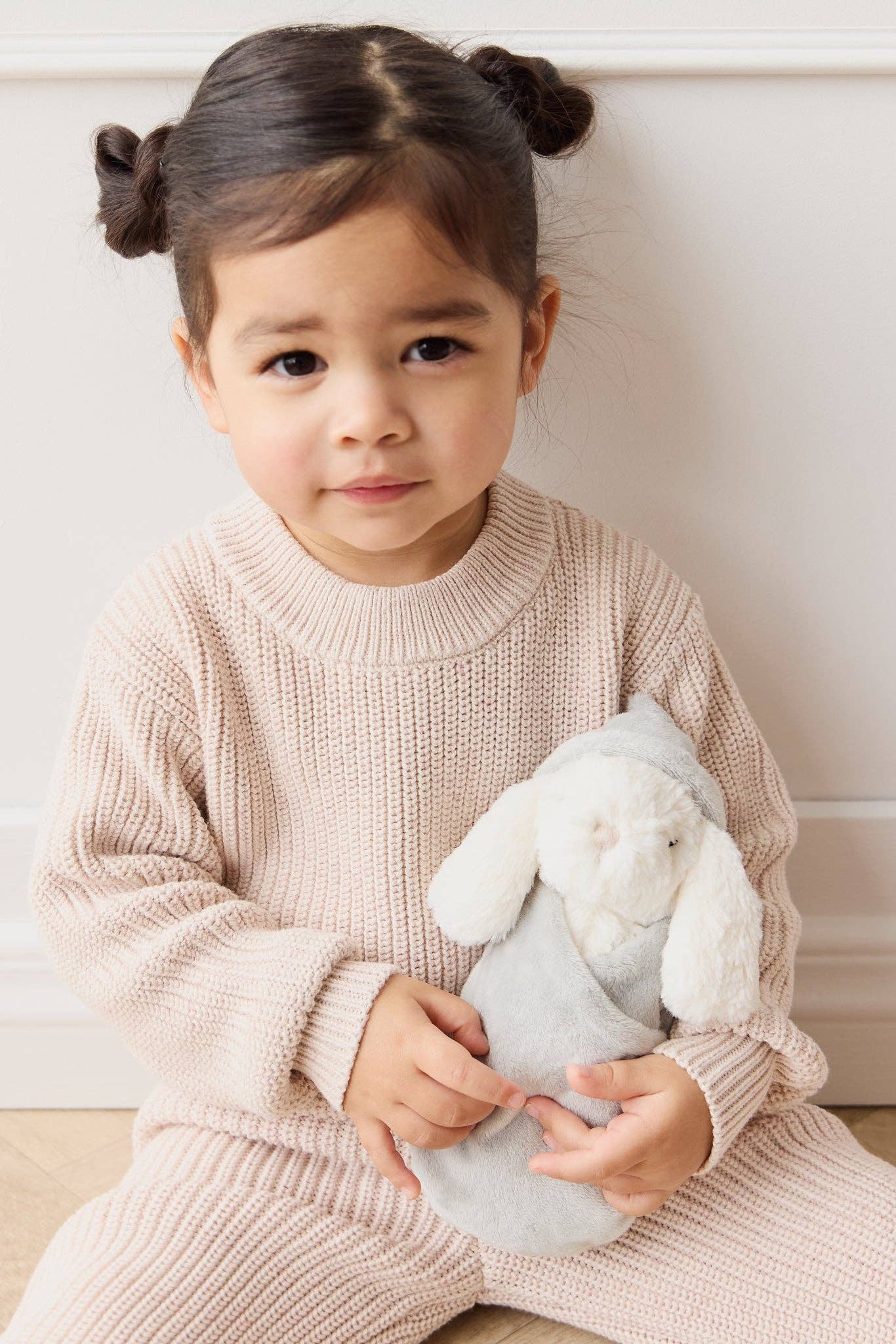 
                  
                    Child in a beige sweater holding a plush bunny toy against a white background.
                  
                