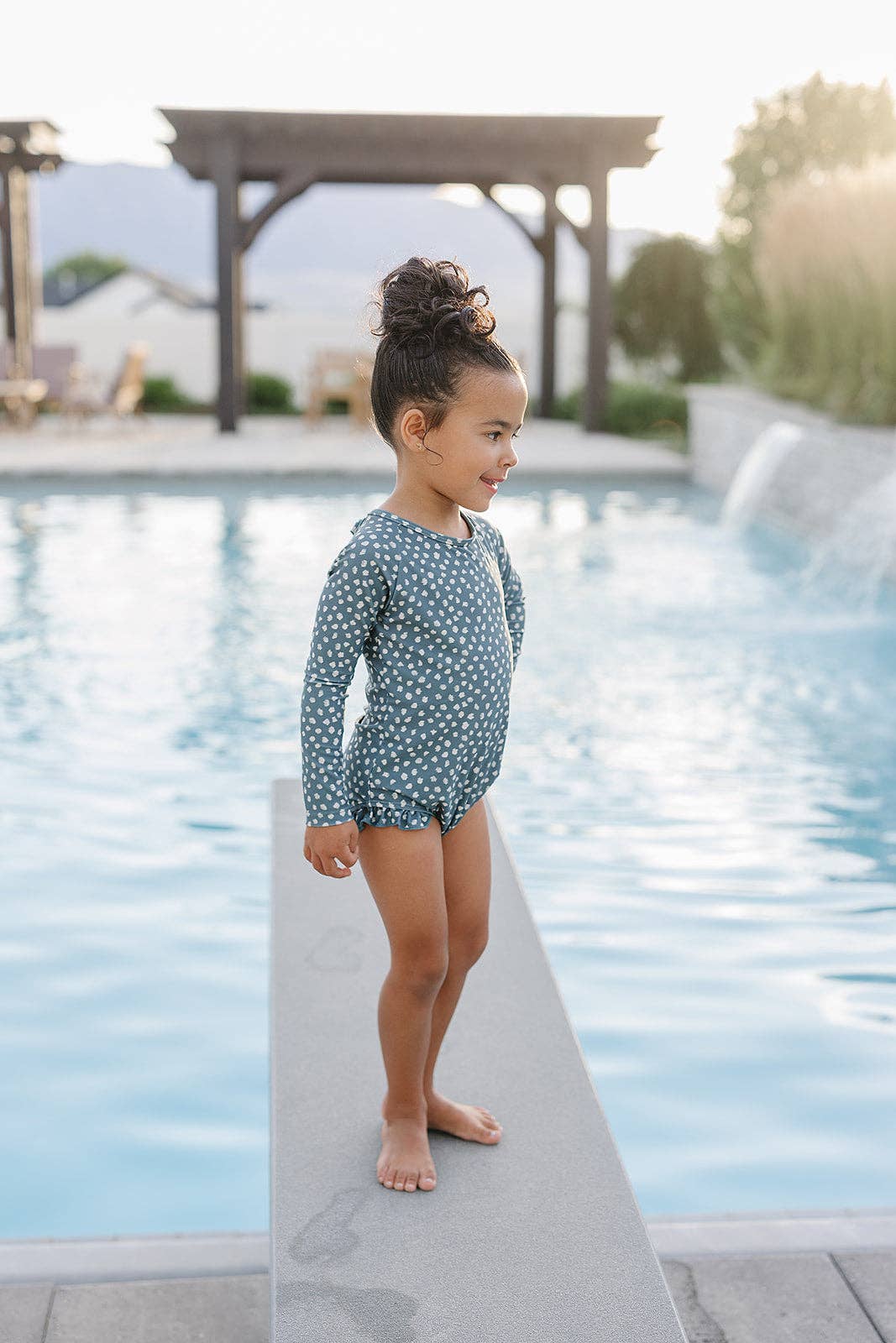 
                  
                    Child in a blue polka dot swimsuit standing by a pool
                  
                