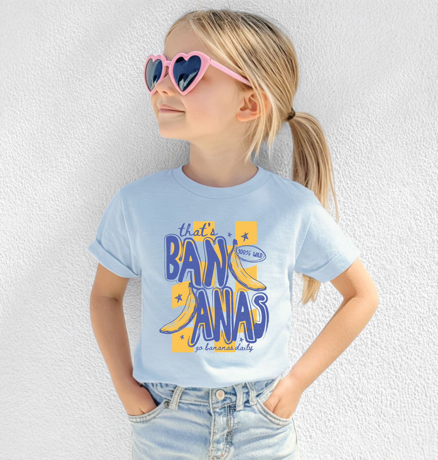 Child wearing a light blue t-shirt with colorful text and sunglasses against a white background.