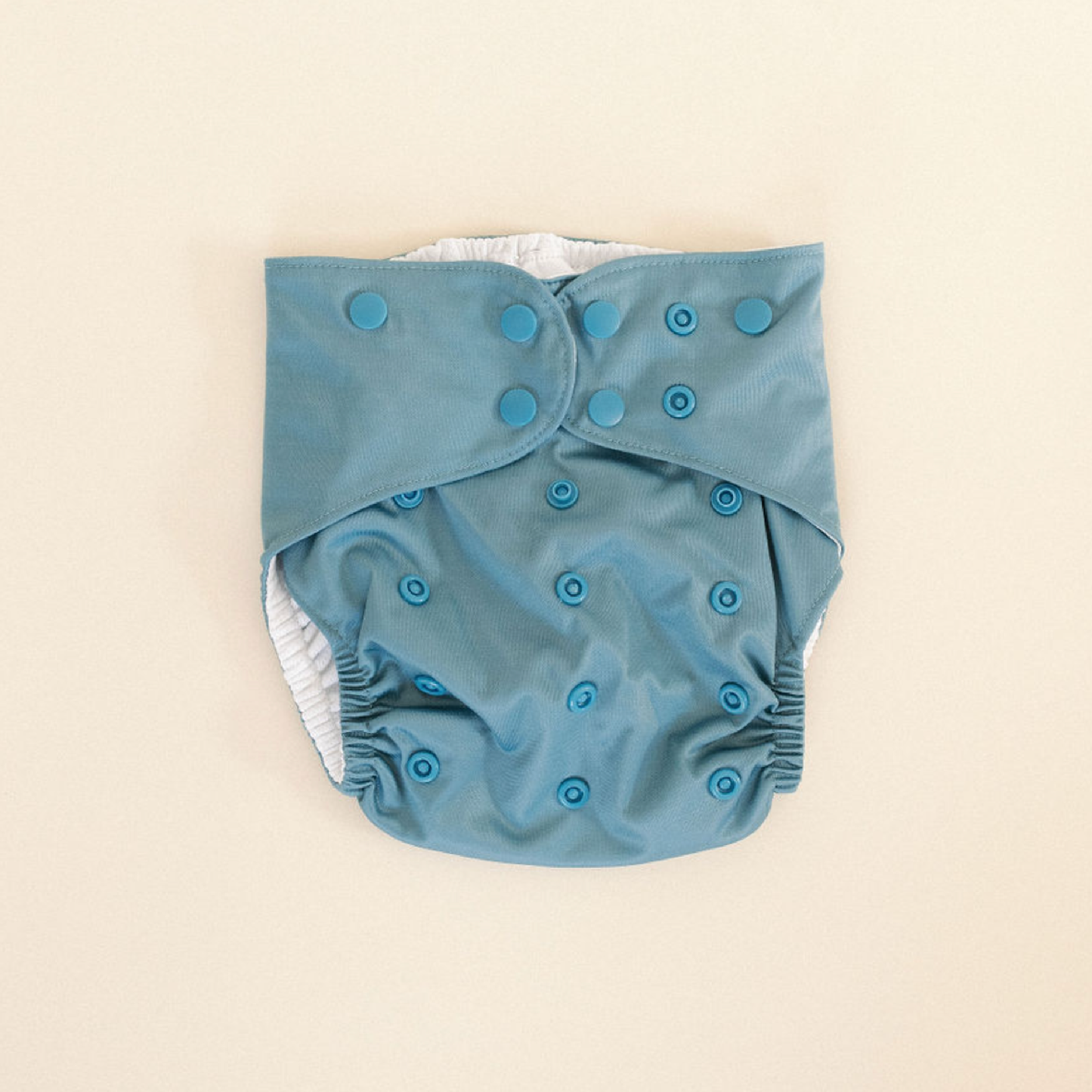 Blue cloth swim diaper with button closures on a beige background.