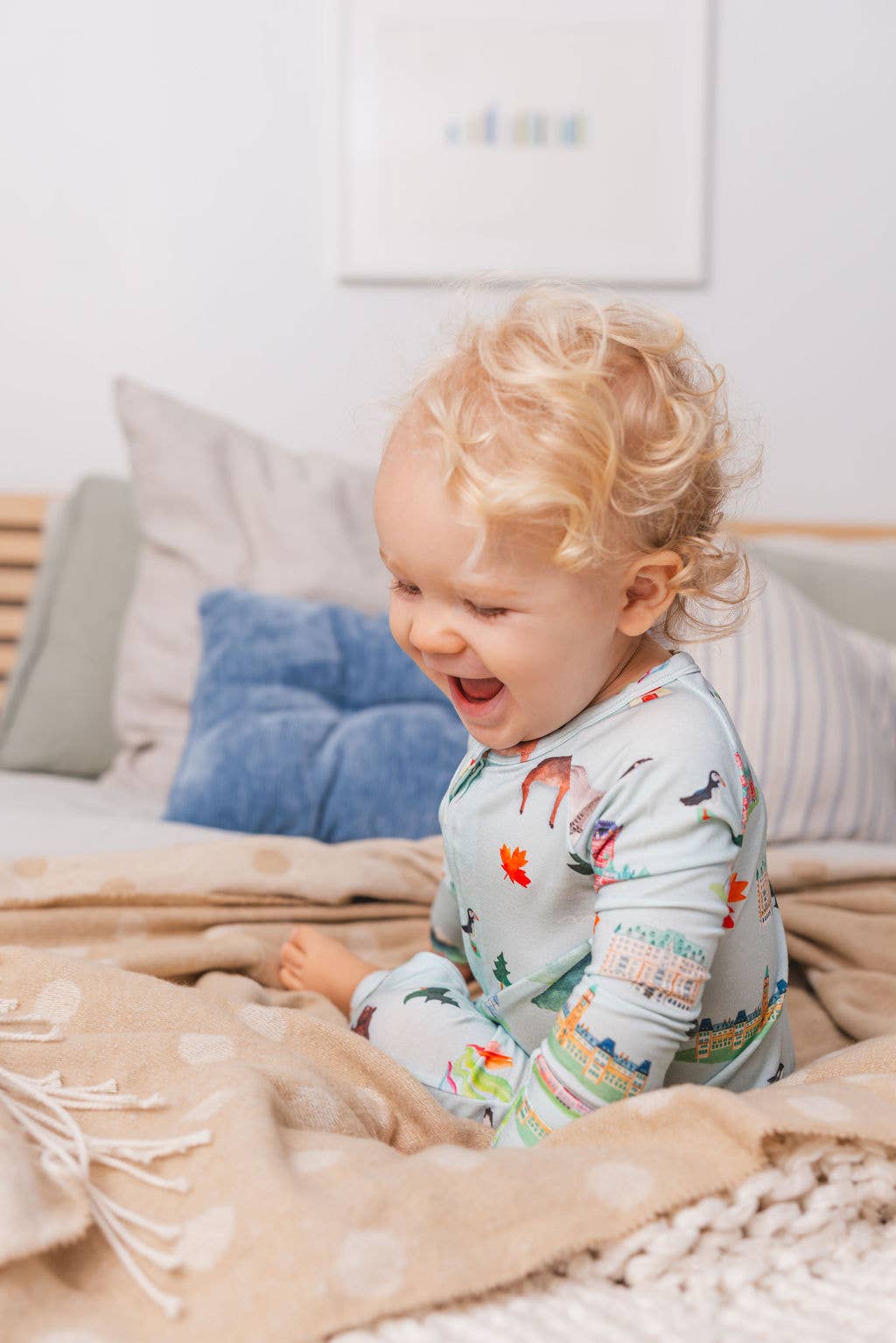 Child in pajamas sitting on a bed with pillows and blankets.