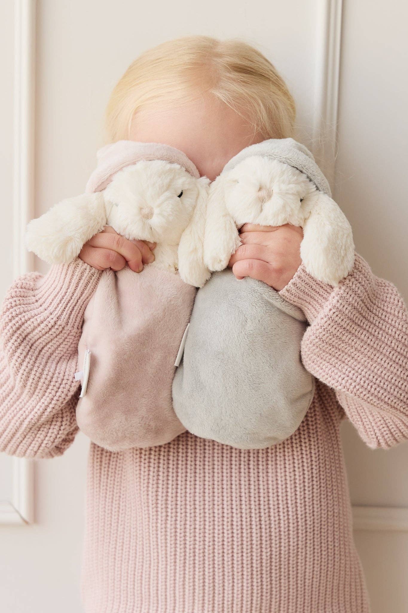 
                  
                    Child holding two plush toys against a white background.
                  
                