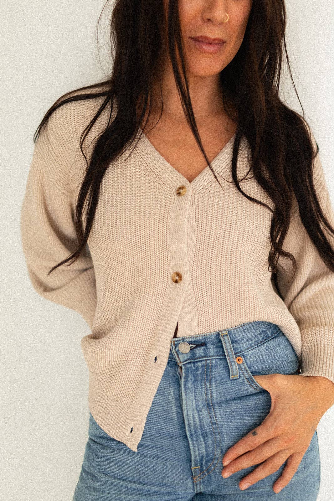 Woman wearing a beige cardigan and blue jeans against a plain background