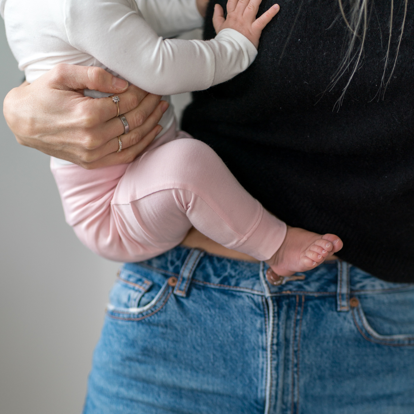 
                  
                    Person holding a child wearing pink pants and a black top against a neutral background.
                  
                