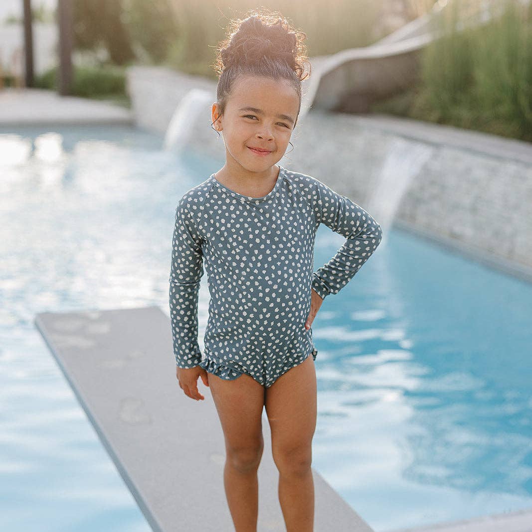 Child in a polka dot swimsuit standing by a pool