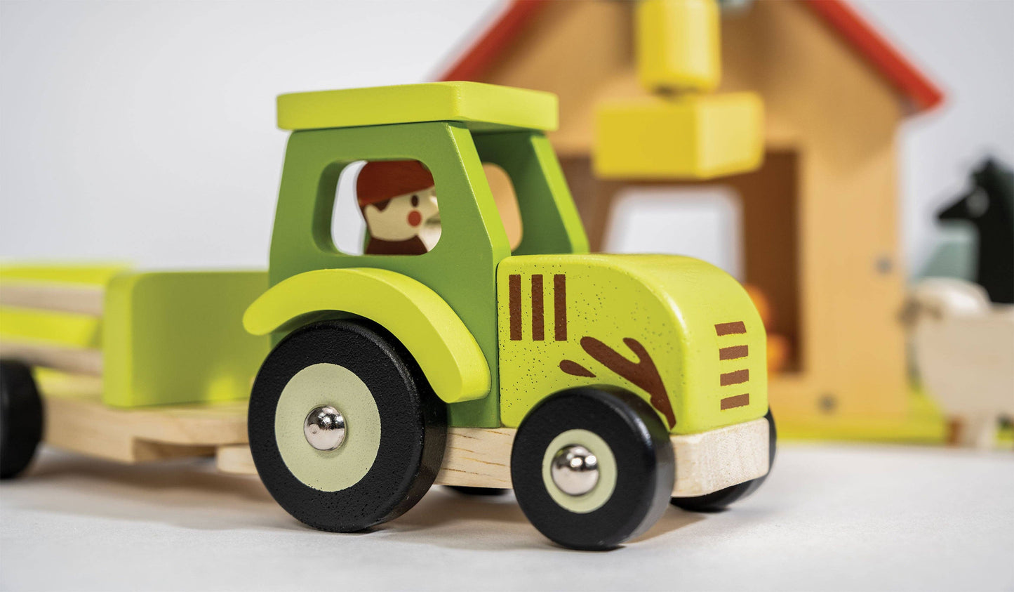 
                  
                    Wooden toy tractor with a driver figure in front of a small wooden house.
                  
                
