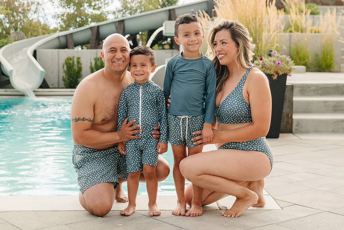 
                  
                    Family of four in matching blue polka dot swimwear posing by a pool. 
                  
                