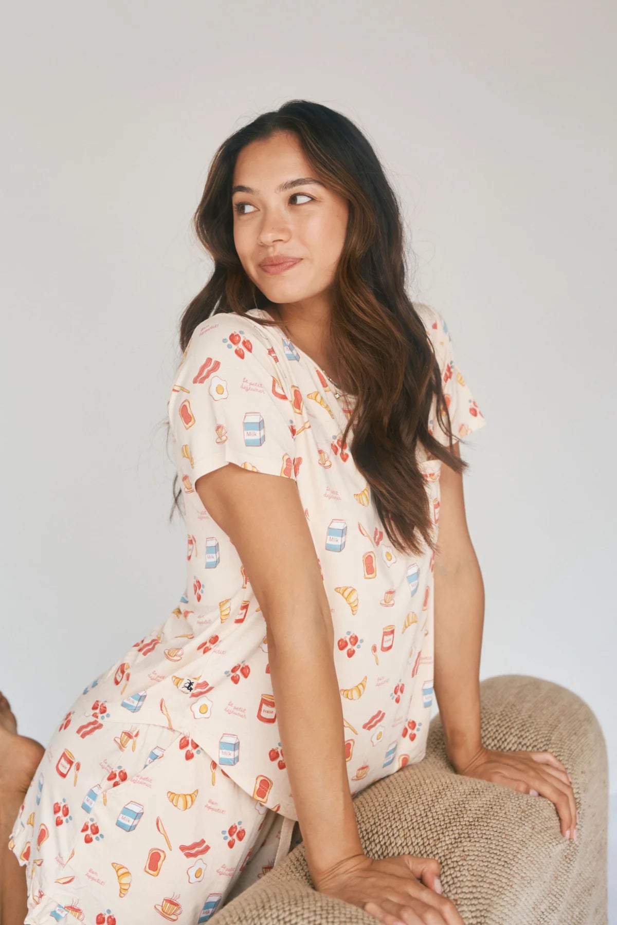 
                  
                    Woman wearing a patterned pajama set sitting on a textured surface with a plain background.
                  
                
