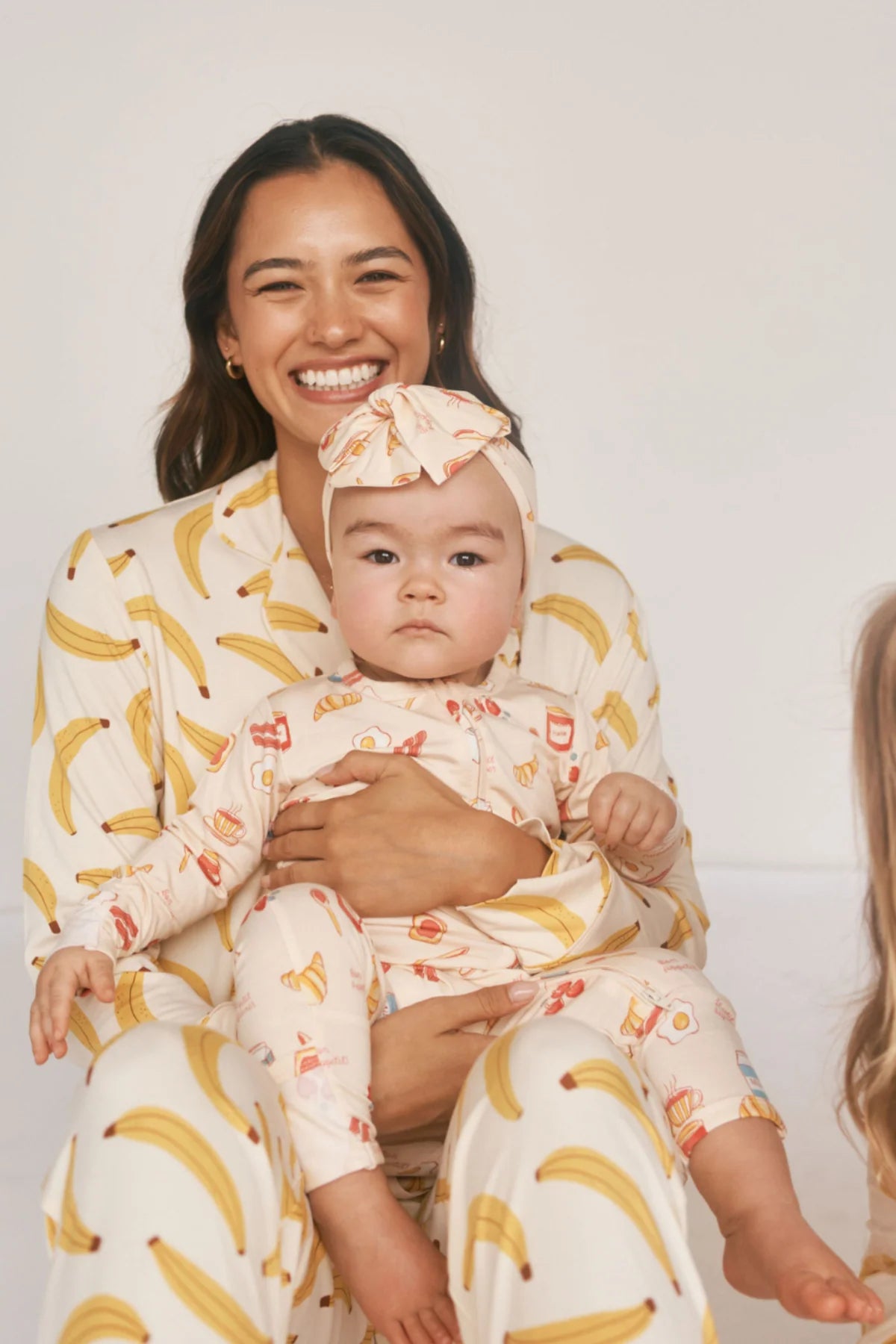 Person holding child wearing a headband with a breakfast foods print against a white background. 