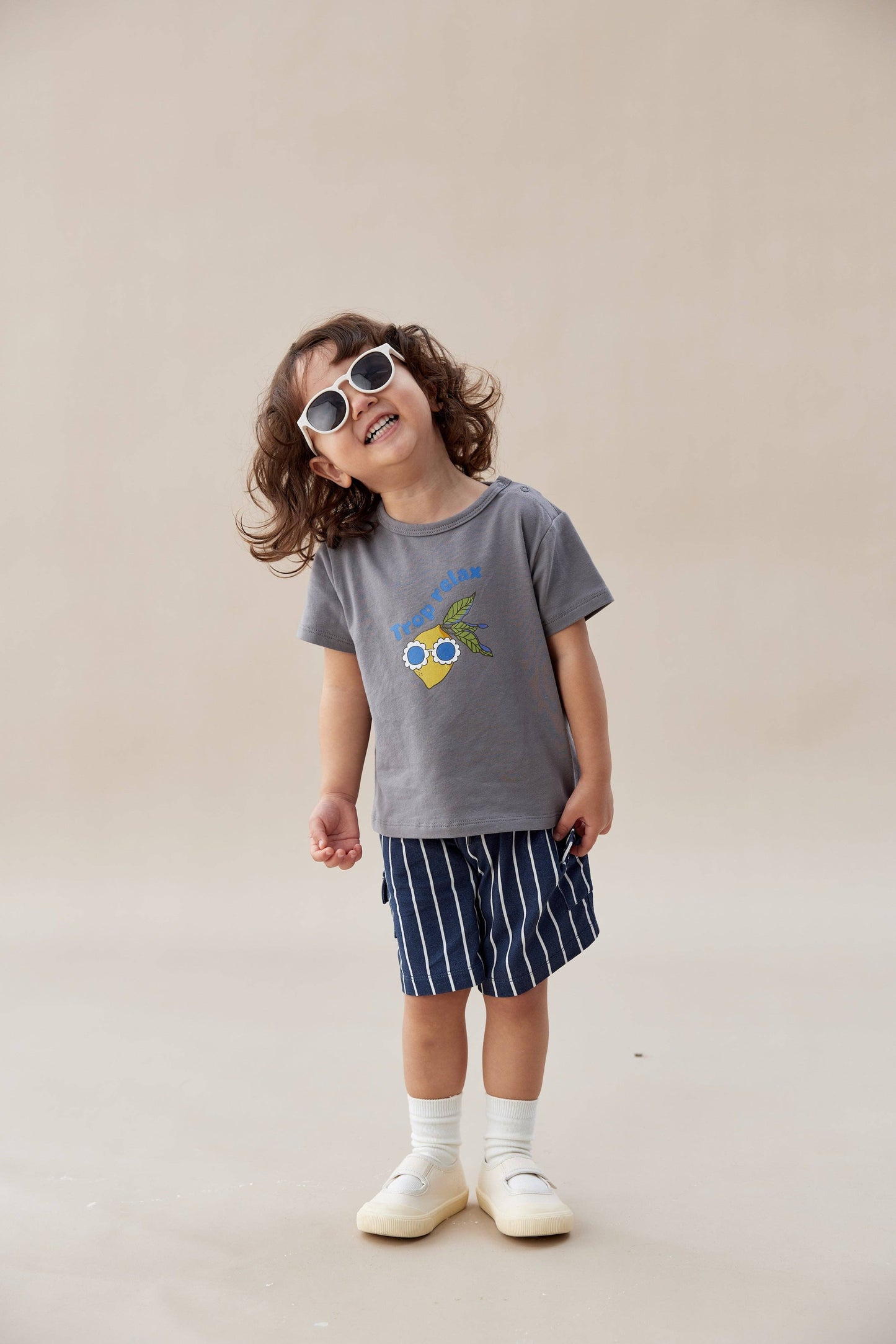 
                  
                    Child wearing a gray t-shirt with a graphic design and striped shorts on a beige background.
                  
                