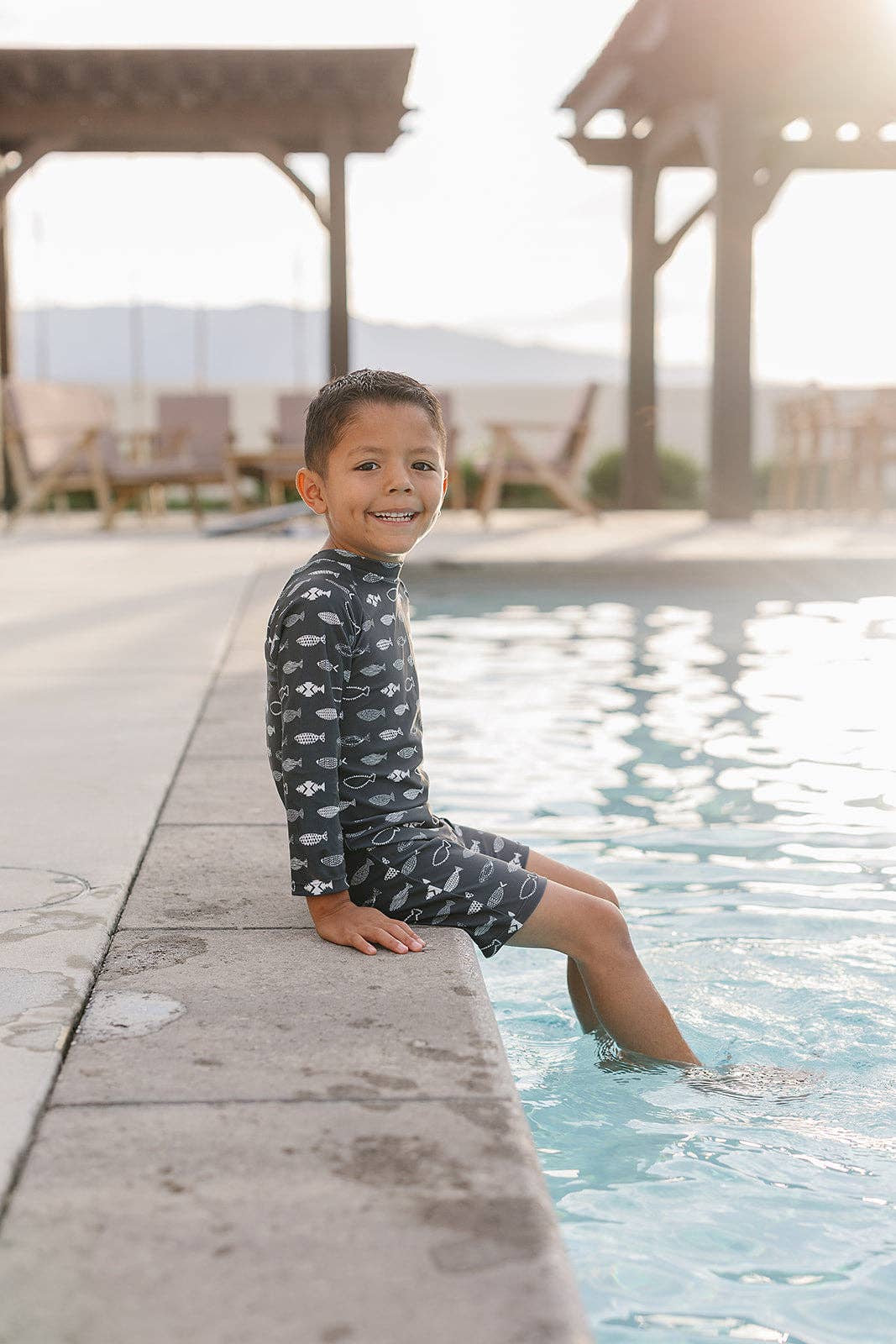
                  
                    Child in a patterned swimsuit sitting by a pool with a gazebo in the background
                  
                