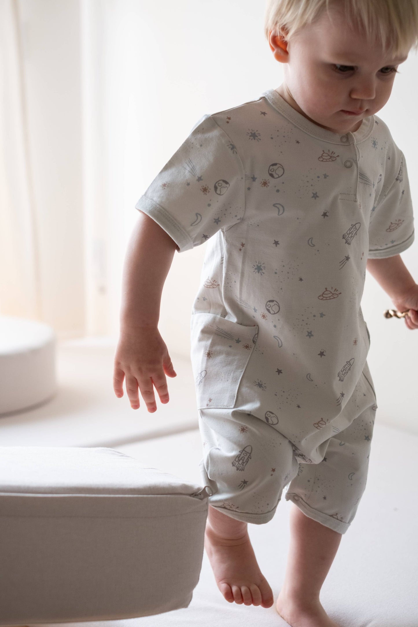 
                  
                    Child wearing a light-colored outfit with patterns in a softly lit room.
                  
                