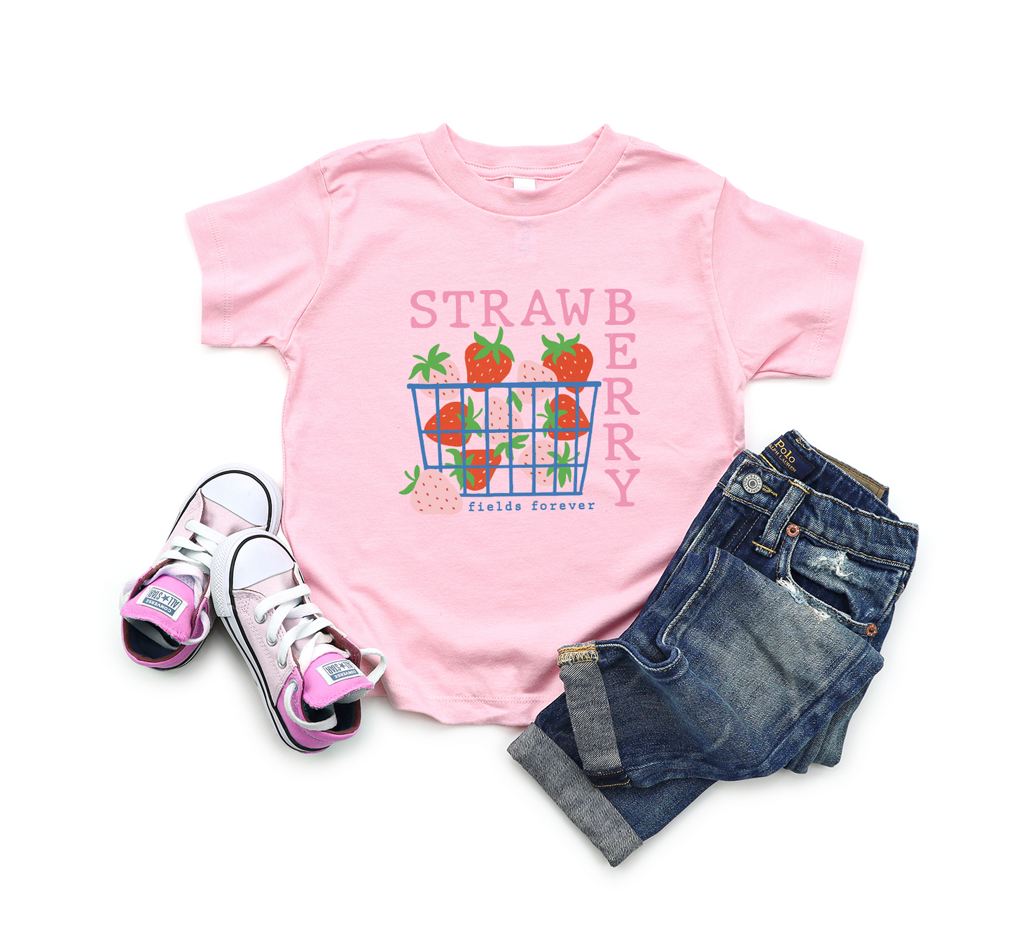 Pink t-shirt with strawberry graphic and text, paired with jeans and sneakers on a white background.