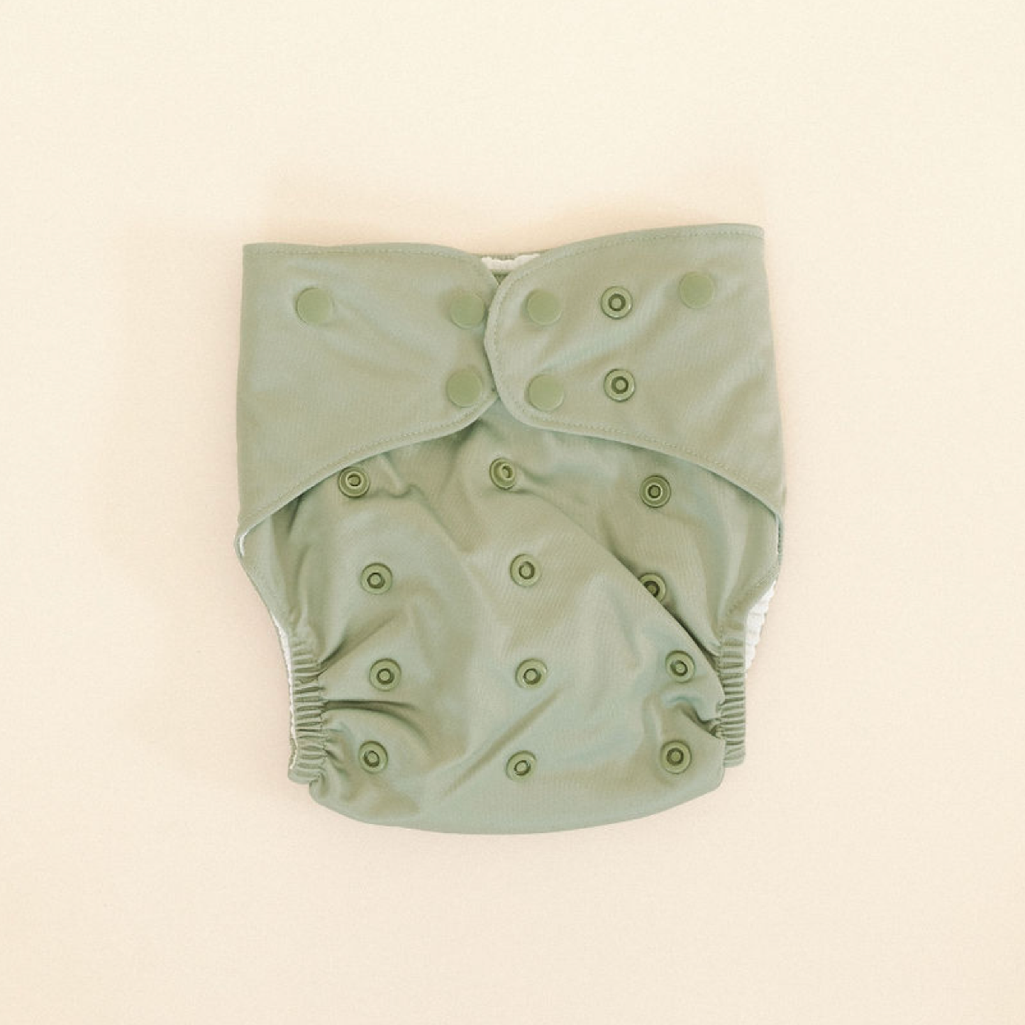 
                  
                    Green baby swim diaper with button closures on a beige background.
                  
                