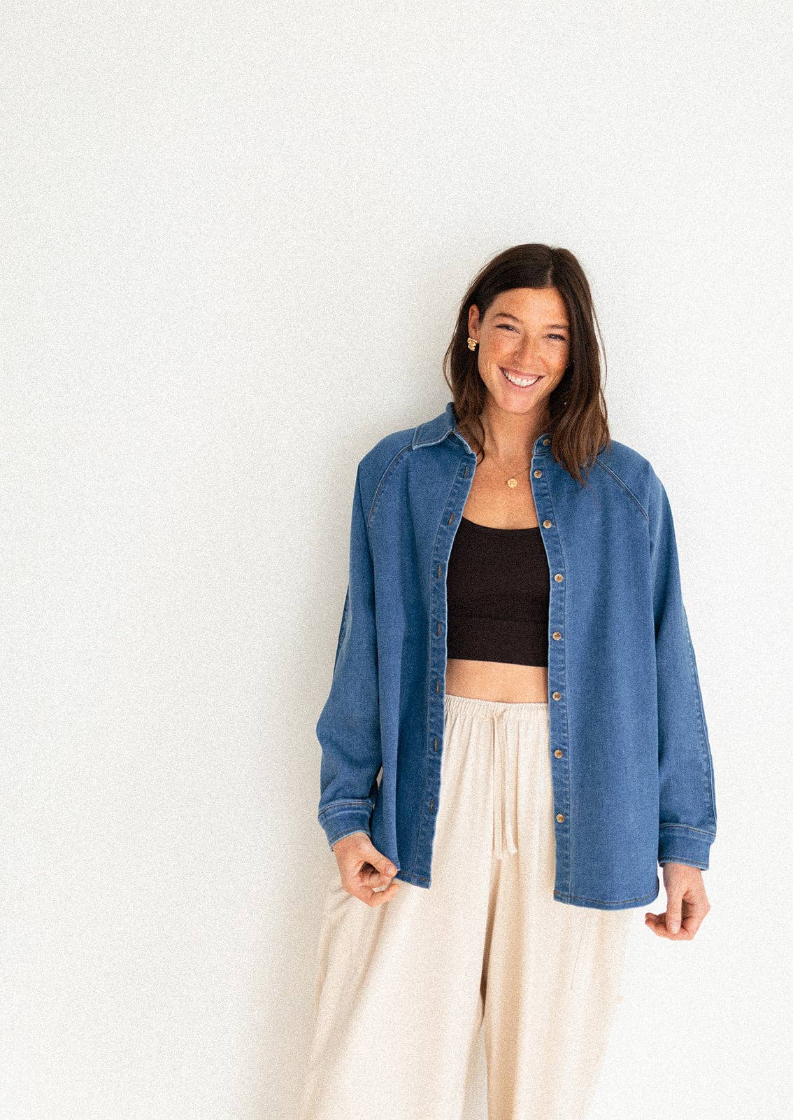 
                  
                    Woman wearing a blue denim shirt over a black crop top and beige pants on a white background
                  
                