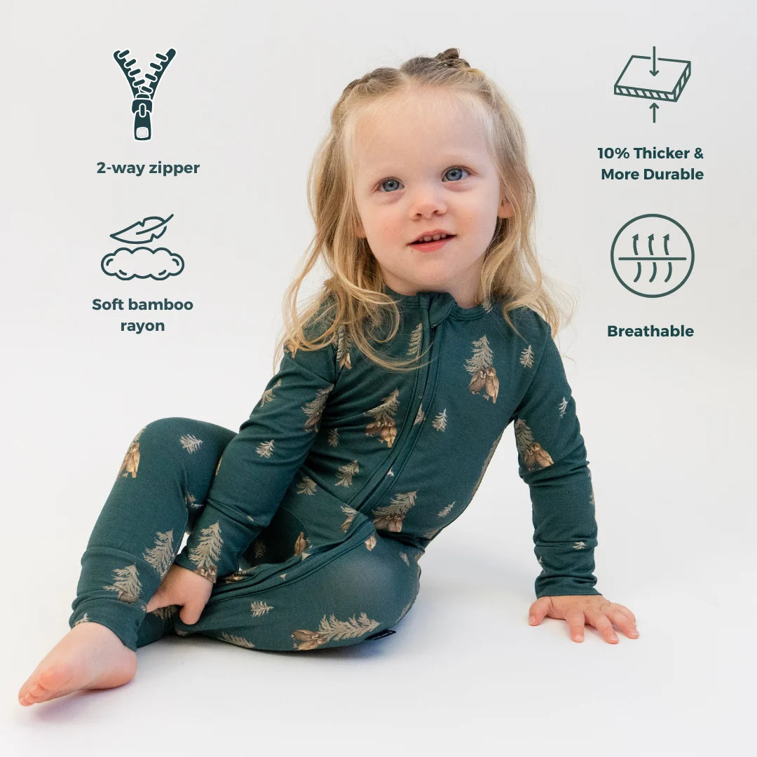 
                  
                    Child sitting in a dark green sleeper featuring a pine tree and owl print against a white background.
                  
                