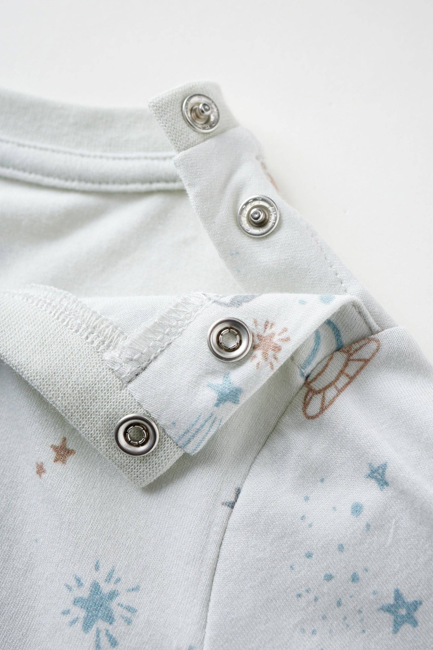 
                  
                    Close-up of a baby outfit with buttons and star pattern on a white background.
                  
                