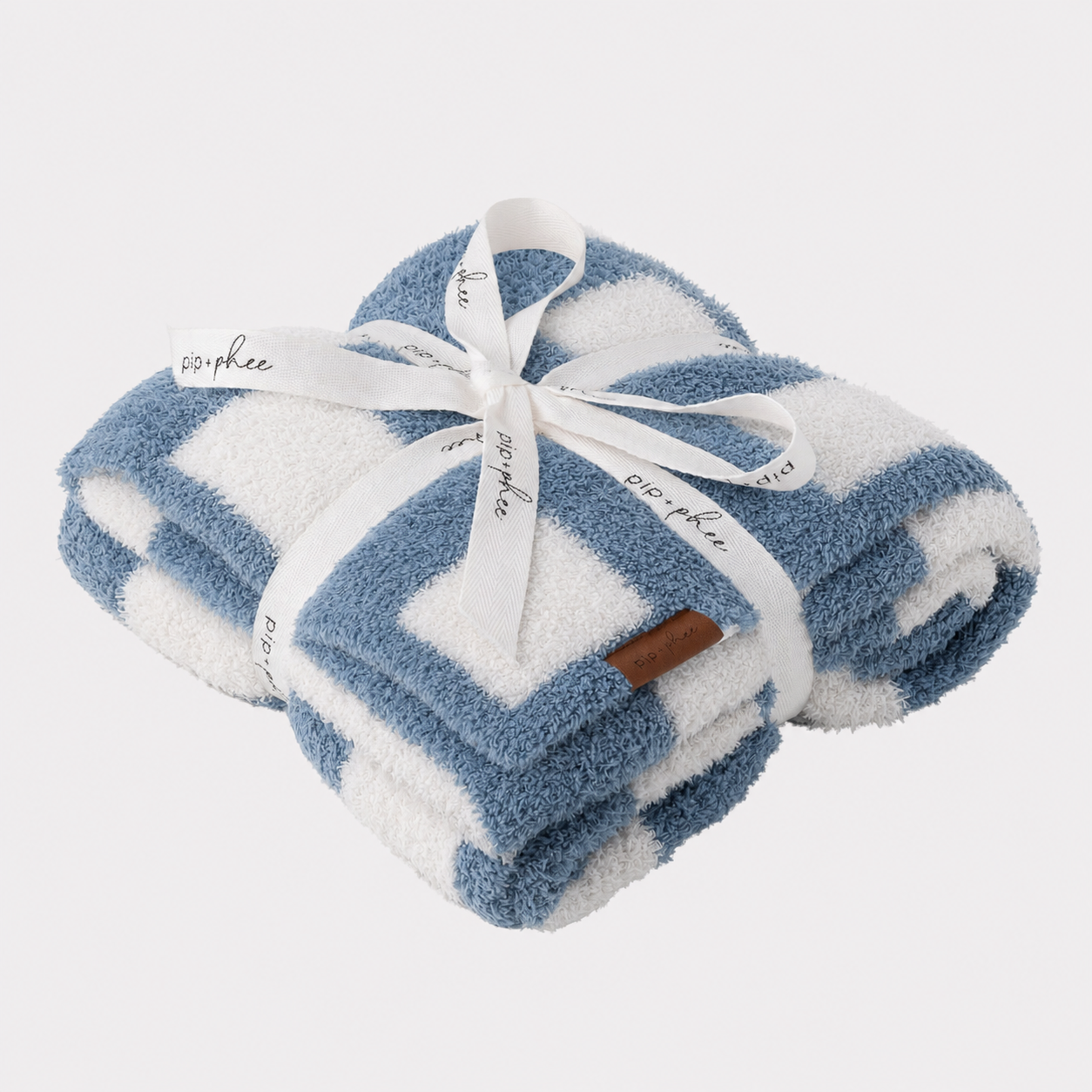 Folded plush blanket with a blue and white geometric pattern, tied together with a white ribbon printed with the brand name 'pip + phee'.