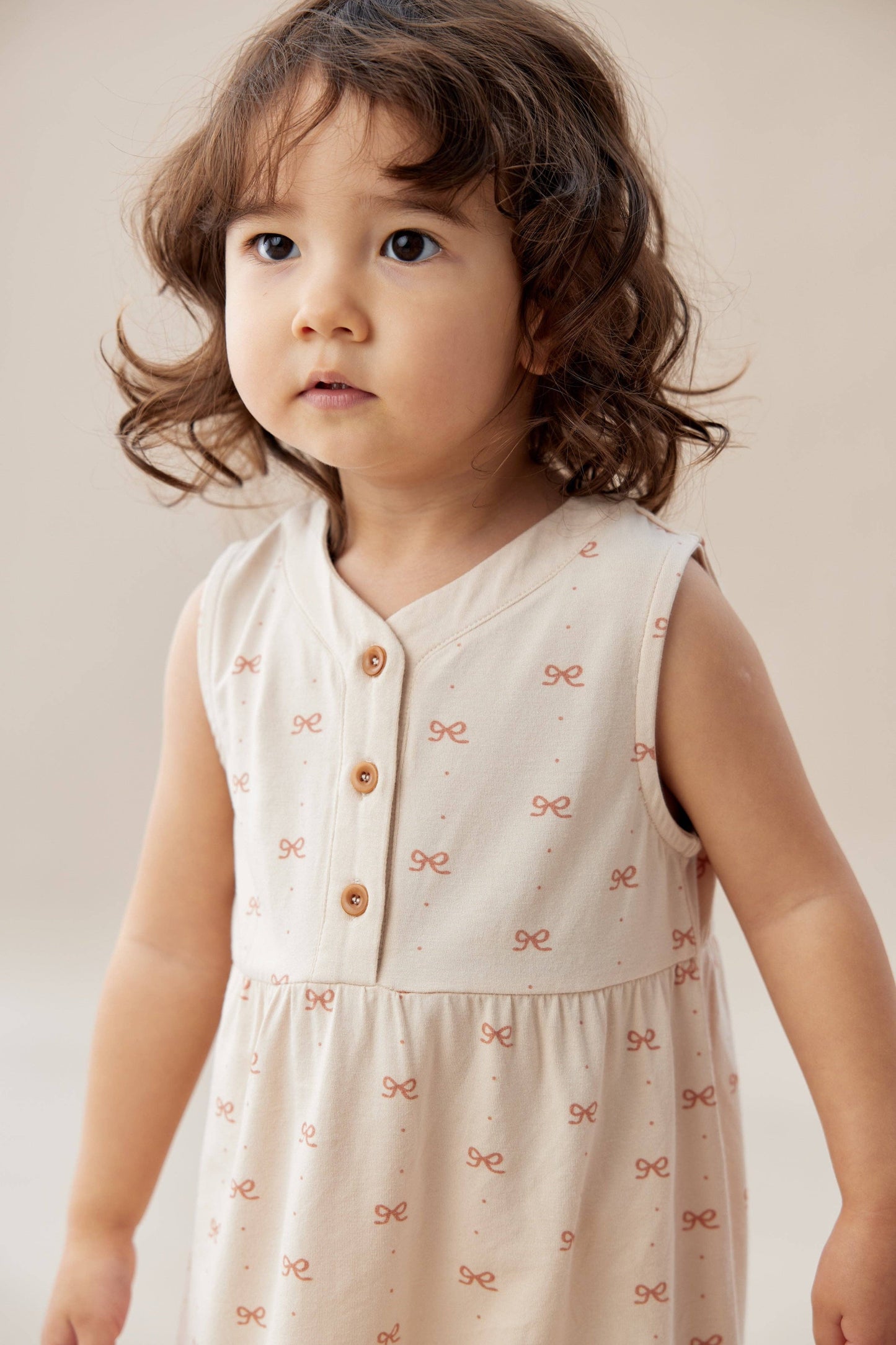 
                  
                    Young child wearing a light-colored dress with small patterns against a neutral background.
                  
                