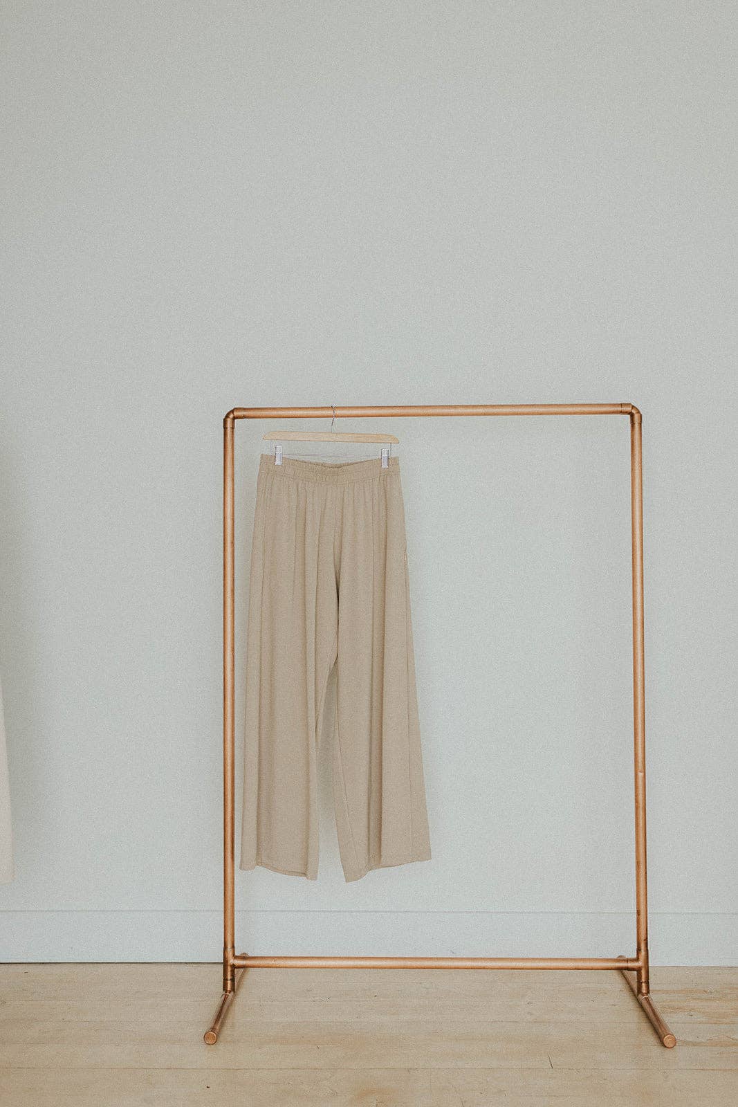 Beige wide leg pants on a copper clothing rack against a light gray wall.