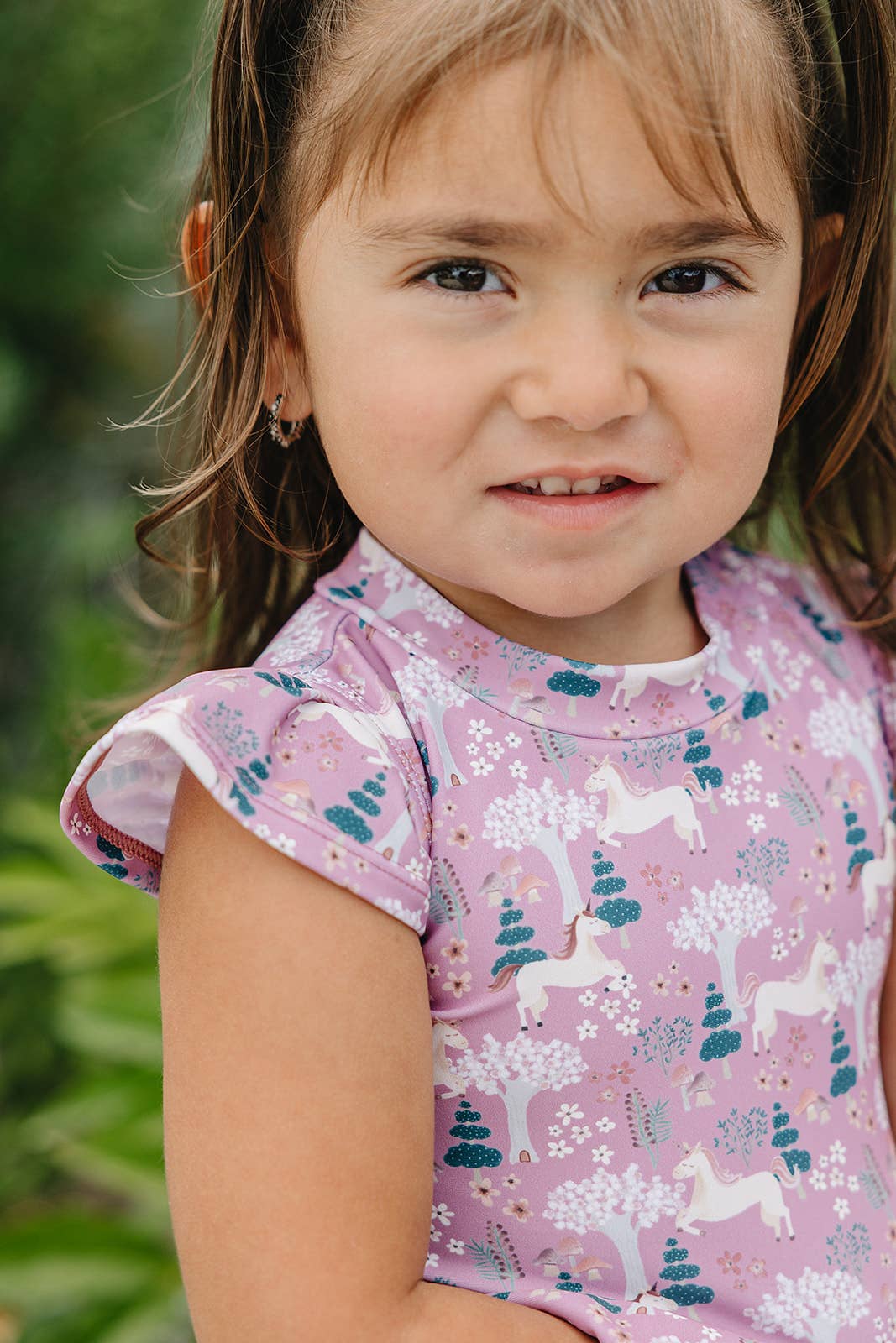 
                  
                    Young girl wearing a pink swimsuit with unicorn design outdoors
                  
                