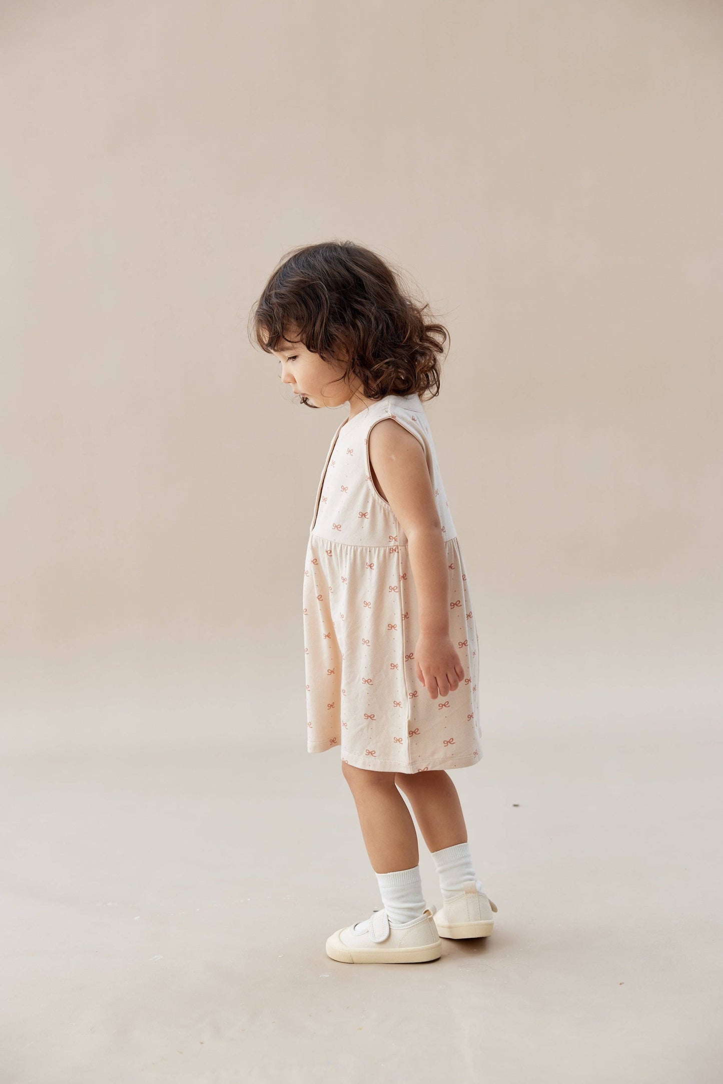 
                  
                    Young child wearing a sleeveless dress with a pattern on a plain background.
                  
                