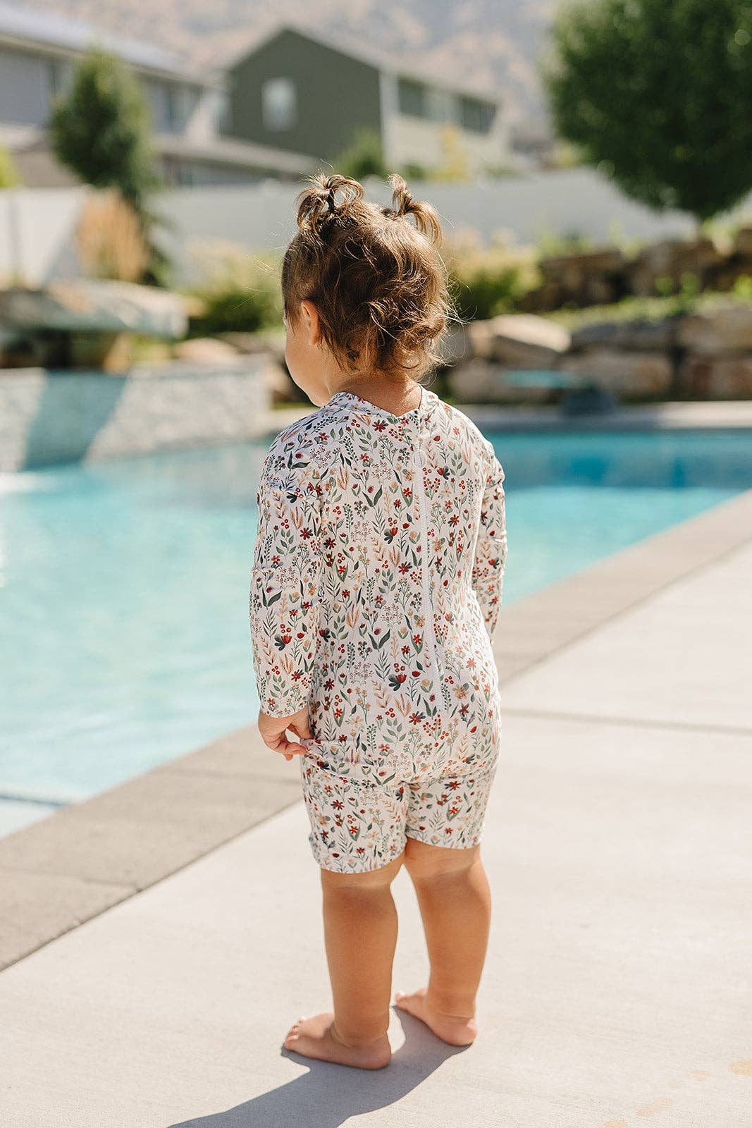 
                  
                    Child in a floral swimsuit standing by a pool with a scenic background
                  
                