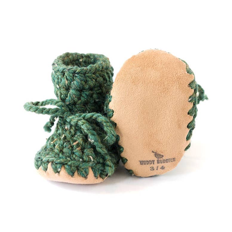 
                  
                    A pair of handmade baby slippers on a white background. One shoe is shown from the front, featuring a green chunky crocheted upper with a matching green laces and a tan suede toe.
                  
                