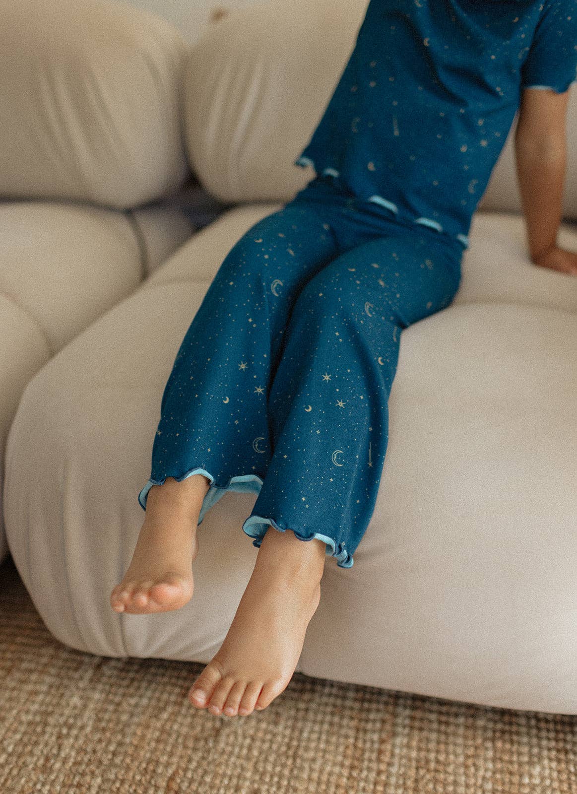 
                  
                    Child wearing blue pants with star print sitting on a beige couch.
                  
                