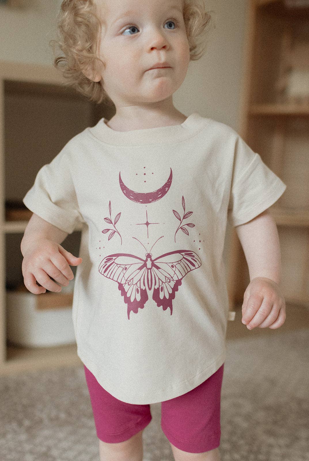 
                  
                    Child wearing a white t-shirt with a purple butterfly design in a room.
                  
                