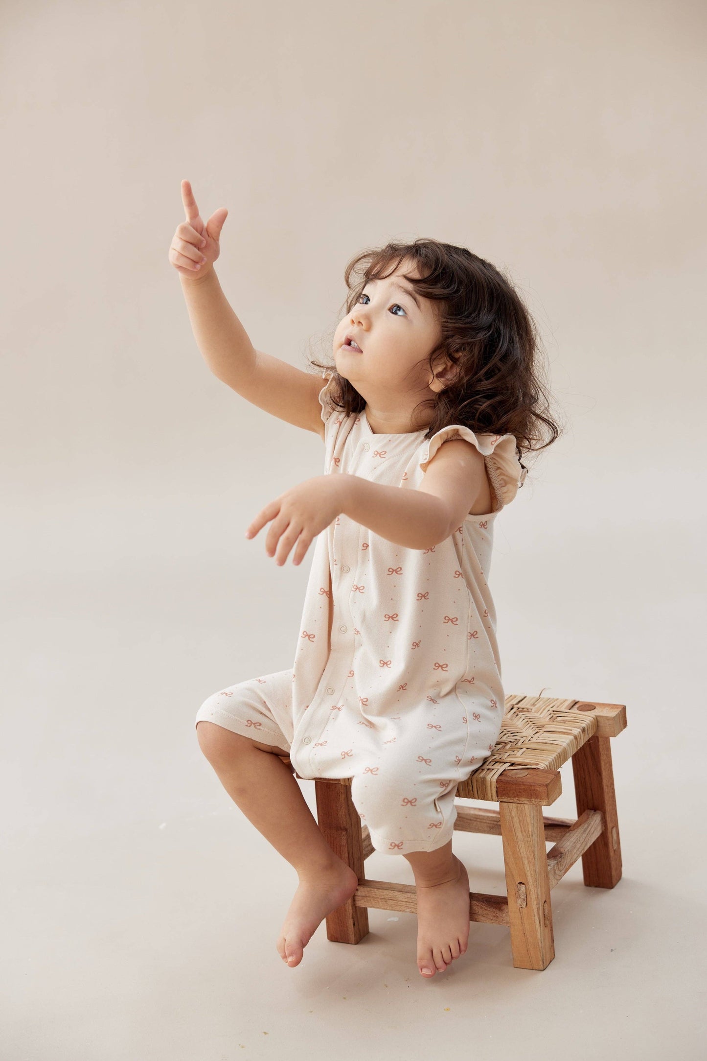 
                  
                    Child sitting on a small wooden stool pointing upwards against a plain background.
                  
                
