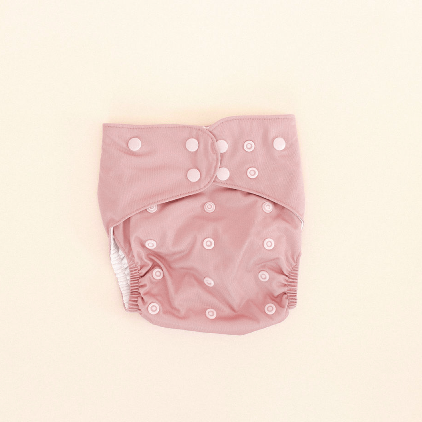 
                  
                    Pink baby swim diaper with white buttons on a beige background.
                  
                