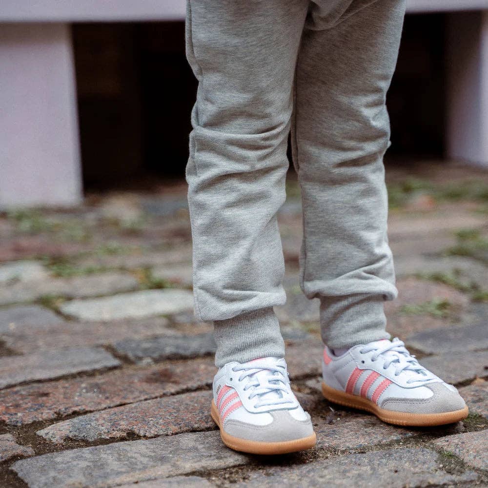 
                  
                    Person wearing gray sweatpants and white sneakers with pink accents on a stone pavement.
                  
                