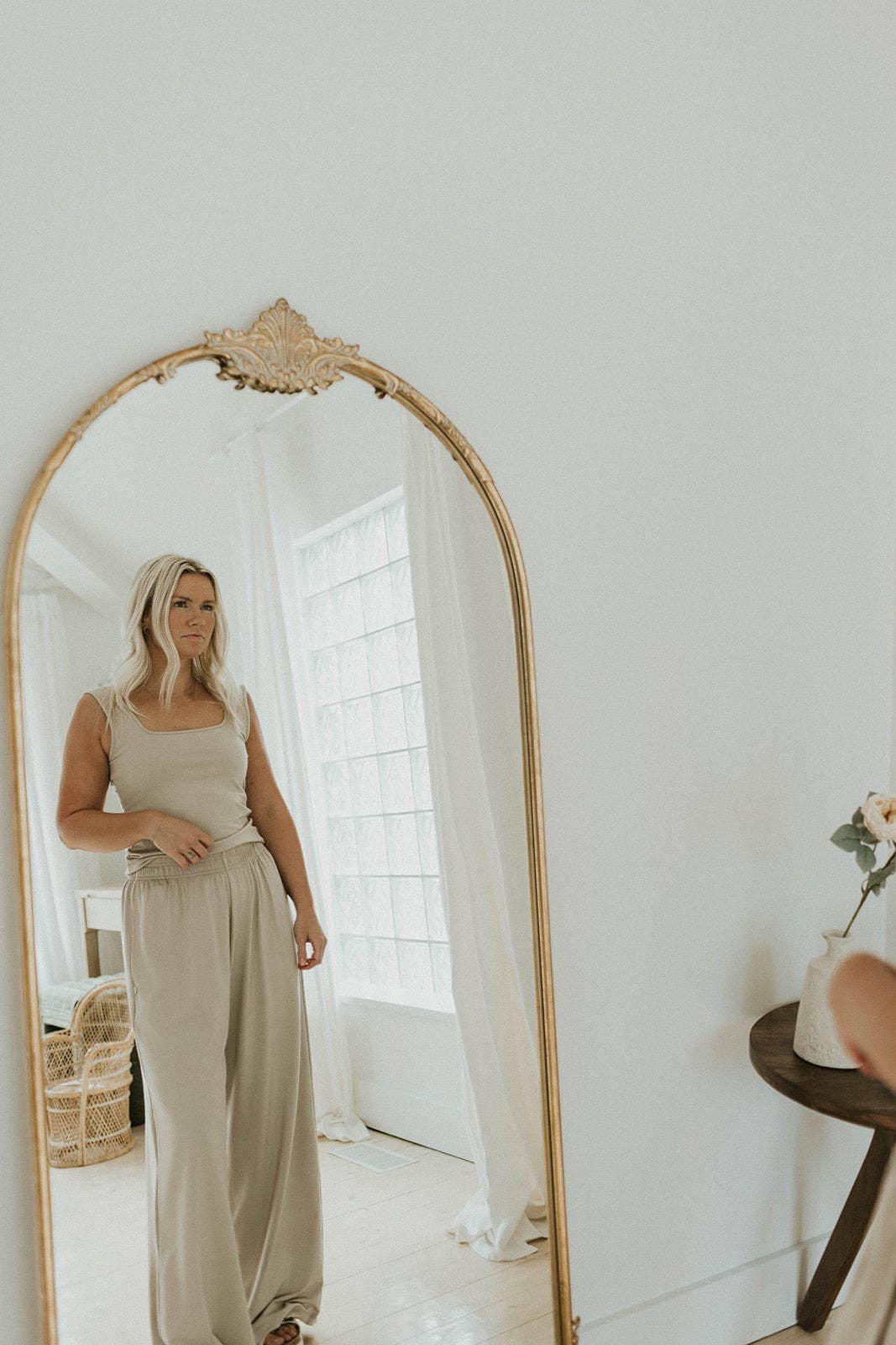 
                  
                    Woman standing in front of a large floor-length mirror in a beige outfit in a bright room.
                  
                