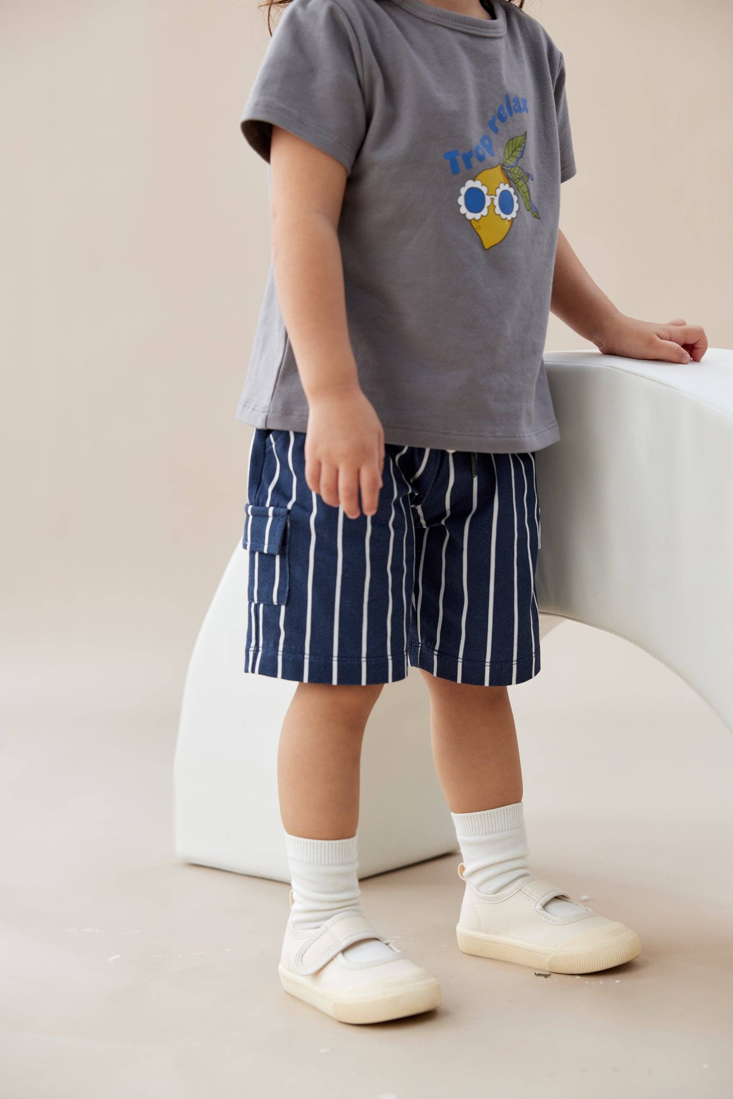 Child wearing a gray t-shirt with a graphic design and blue striped shorts, standing on a light-colored floor.