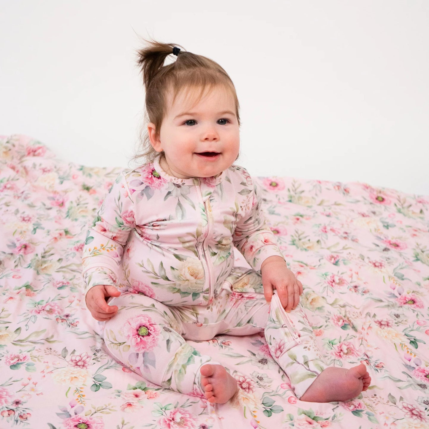 
                  
                    Baby in a floral outfit sitting on a floral blanket.
                  
                