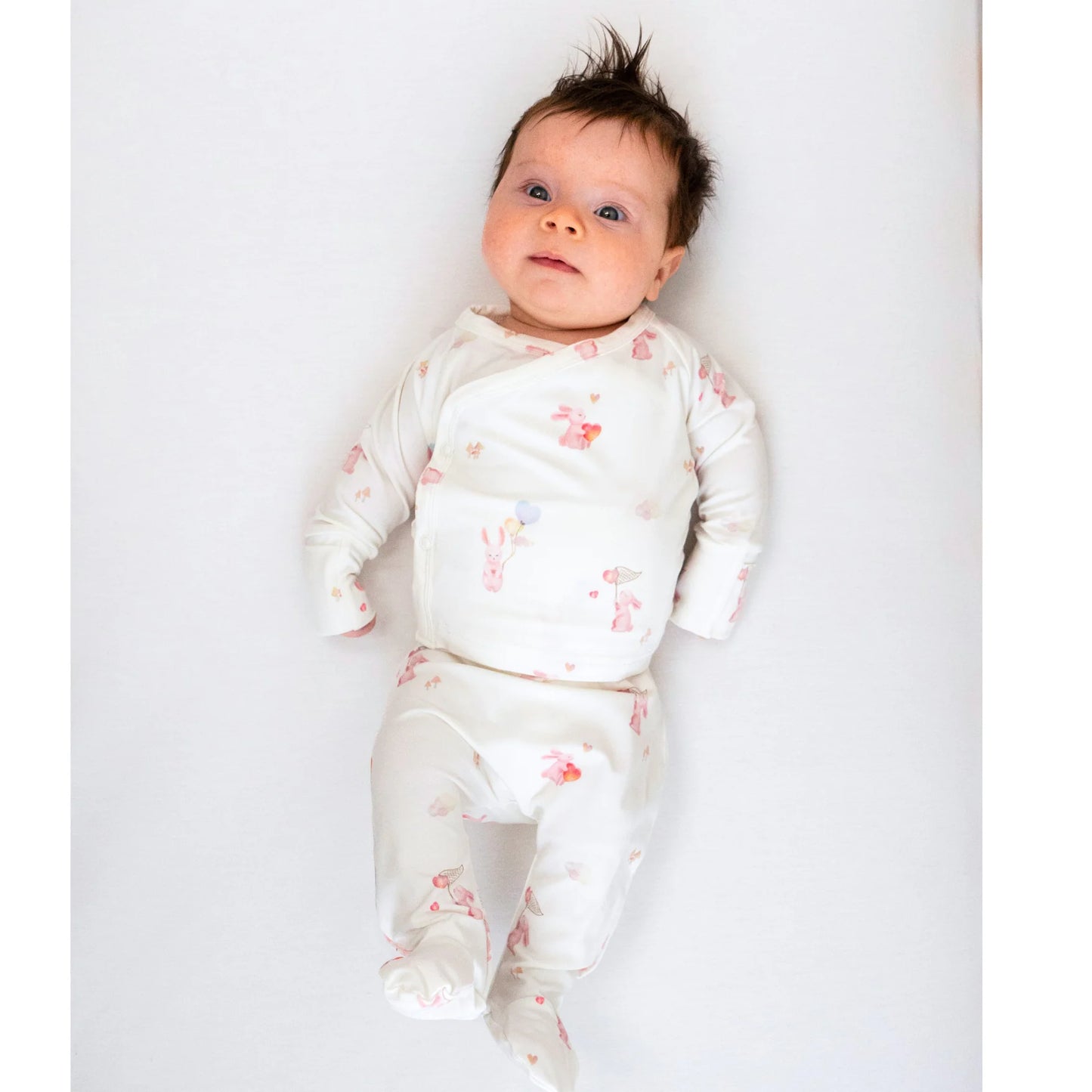 
                  
                    Baby in a white outfit with a bunny print on a white background. 
                  
                