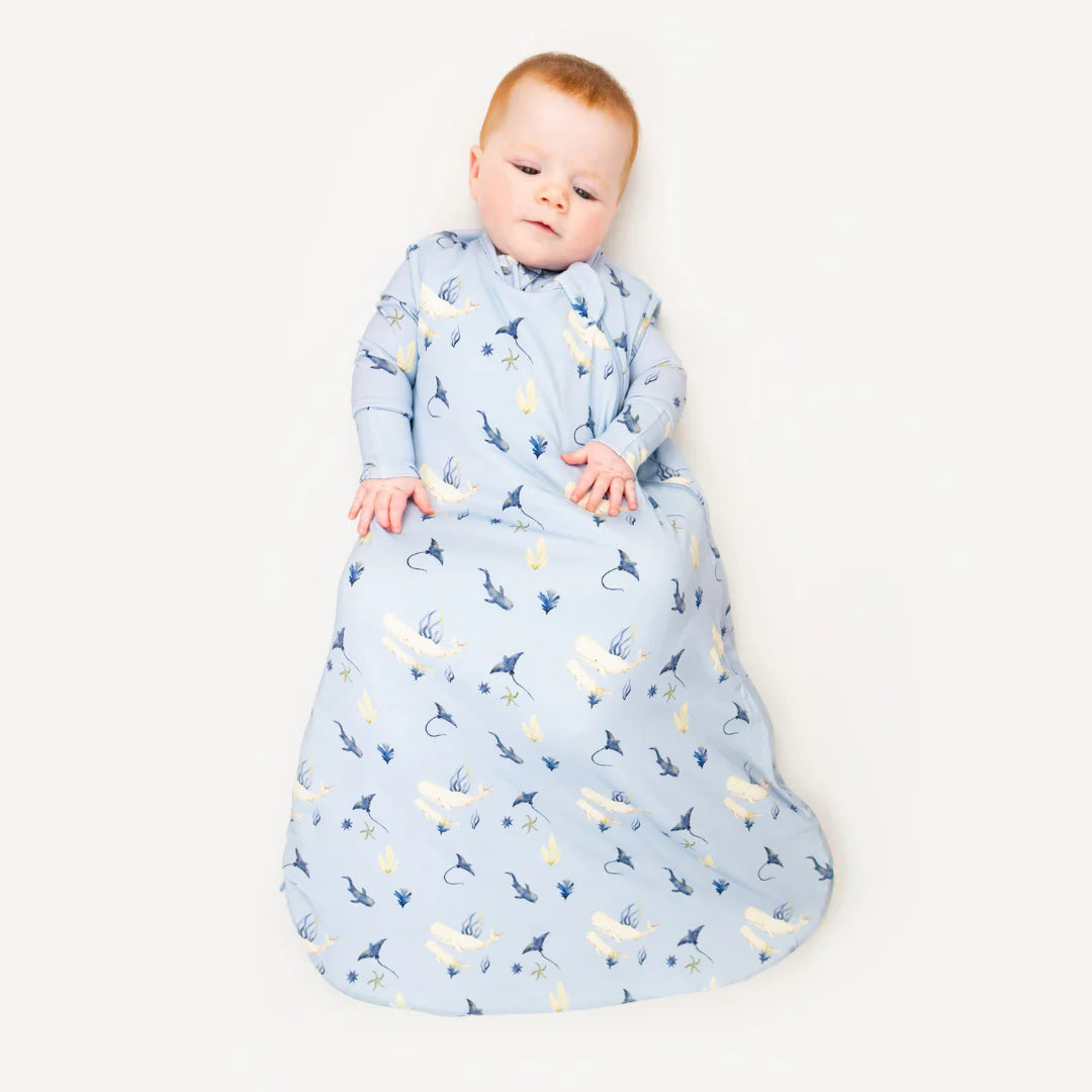 Baby in a blue whale print sleep sack with a white background. 