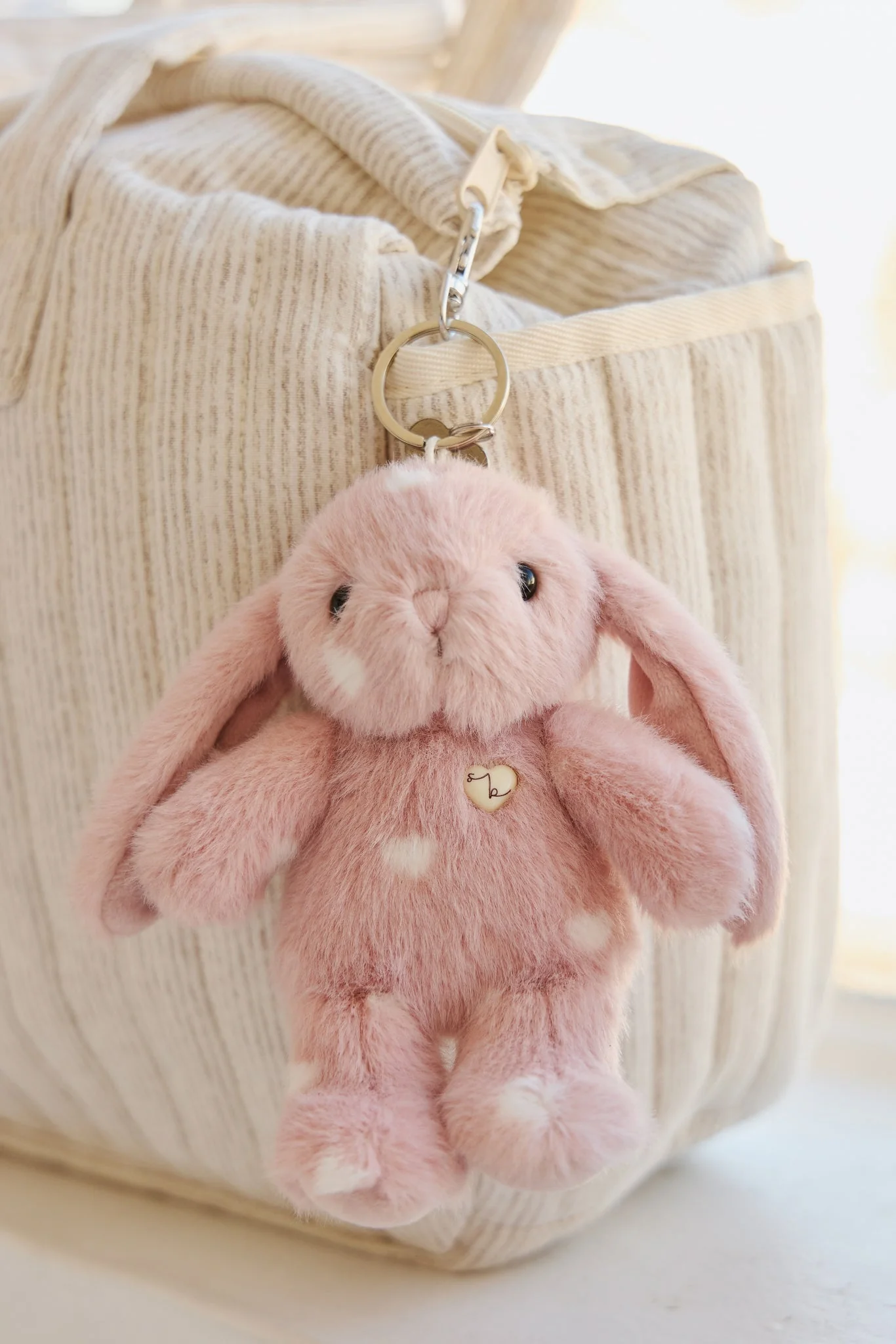 
                  
                    Pink plush bunny keychain attached to a beige bag.
                  
                