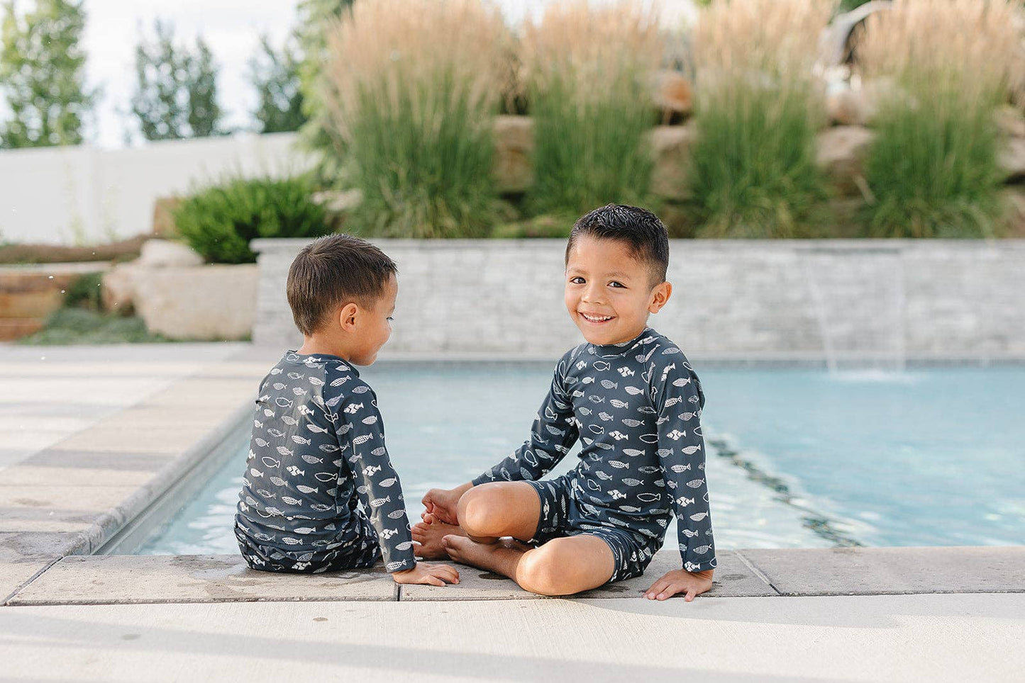 
                  
                    Two children in matching swim shirts sitting by a pool.
                  
                