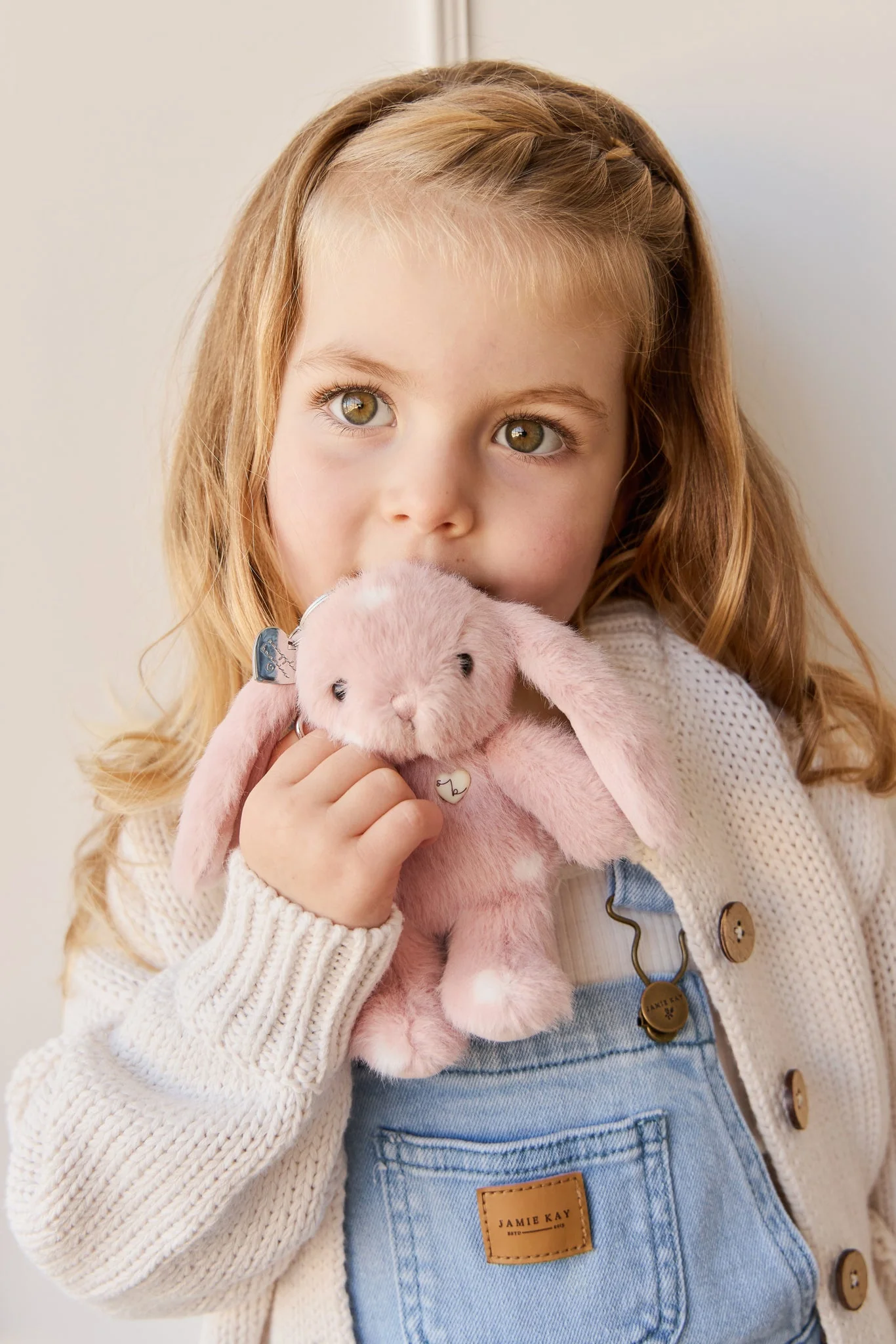 
                  
                    Young girl holding a pink plush bunny toy against a light background.
                  
                