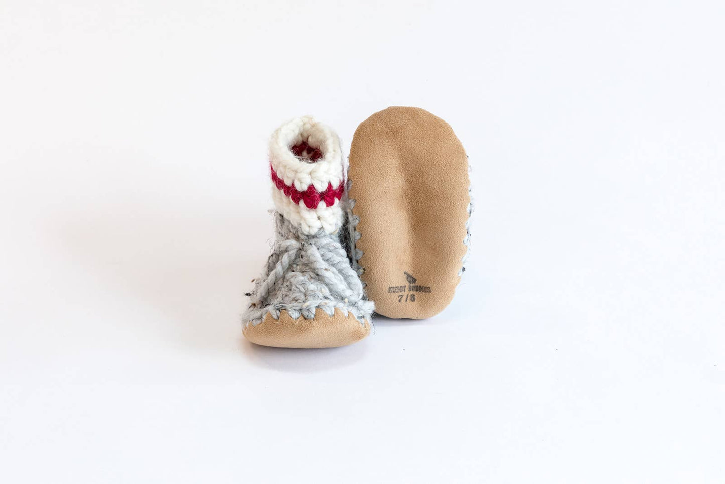 
                  
                    Grey, white and red wool booties with suede soles against a white background. 
                  
                