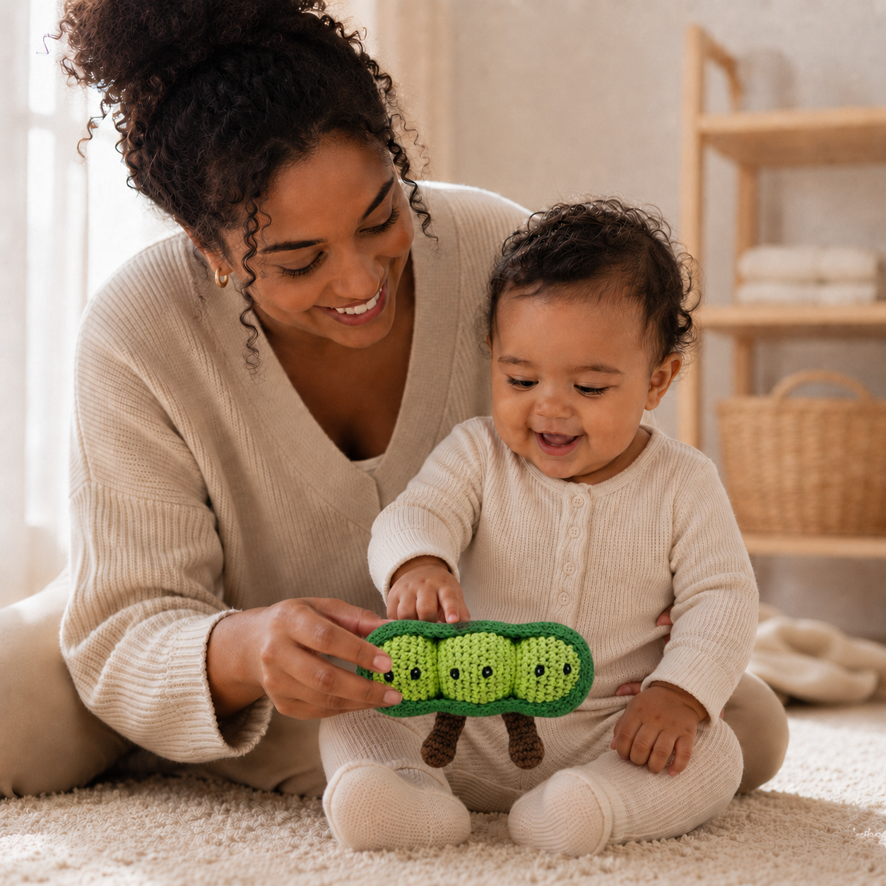 
                  
                    A woman and a baby sit on a carpeted floor in a bright room, smiling as the baby holds a green crocheted pea pod toy.
                  
                
