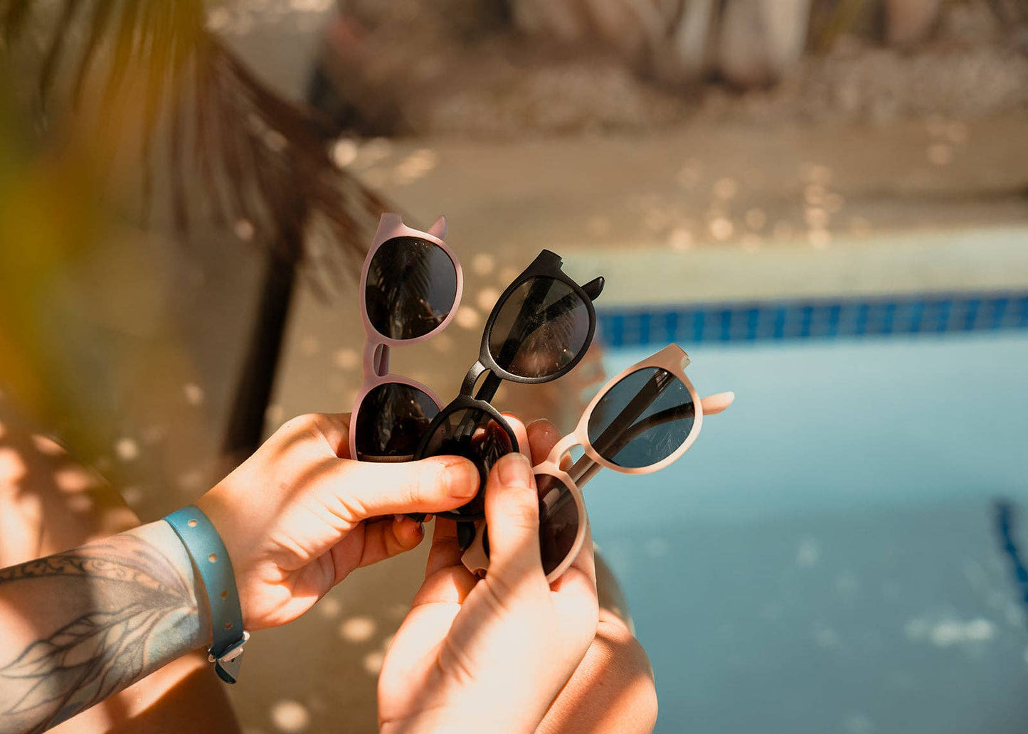 
                  
                    Person holding multiple pairs of sunglasses by a pool.
                  
                