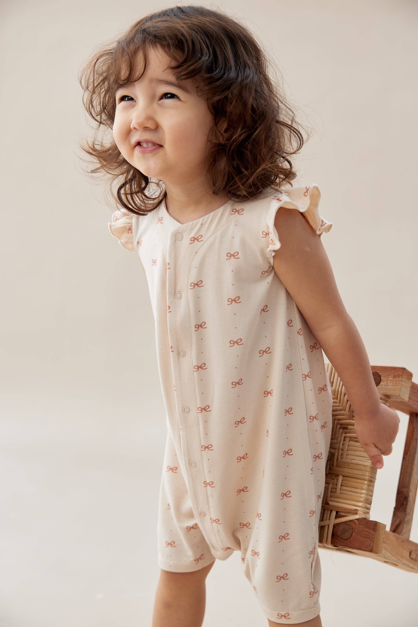 
                  
                    Child wearing a romper with pink patterns, holding a woven basket against a plain background.
                  
                
