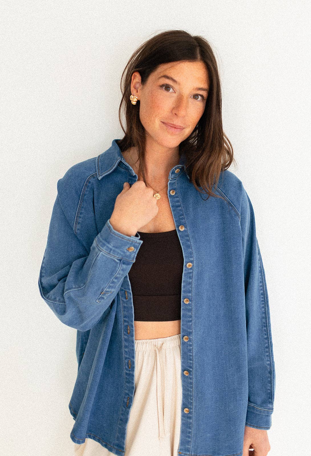 
                  
                    Woman wearing a blue denim jacket over a black top and white pants against a white background
                  
                