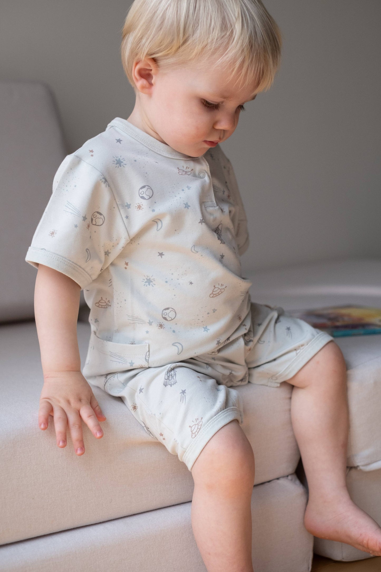 
                  
                    Child wearing a light-colored outfit with small patterns sitting on a couch.
                  
                