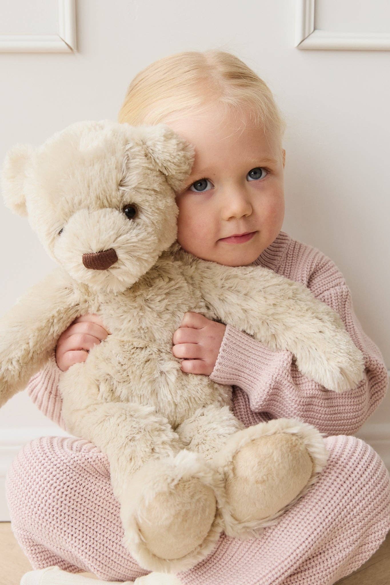 
                  
                    Child holding a teddy bear against a white wall.
                  
                